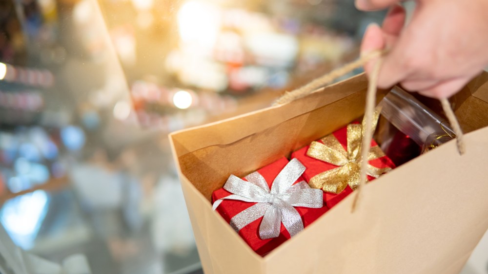 Male hand holding paper shopping bag with red gift boxes inside at Christmas event in department store. Buying present for Xmas holiday and New Year celebration concept