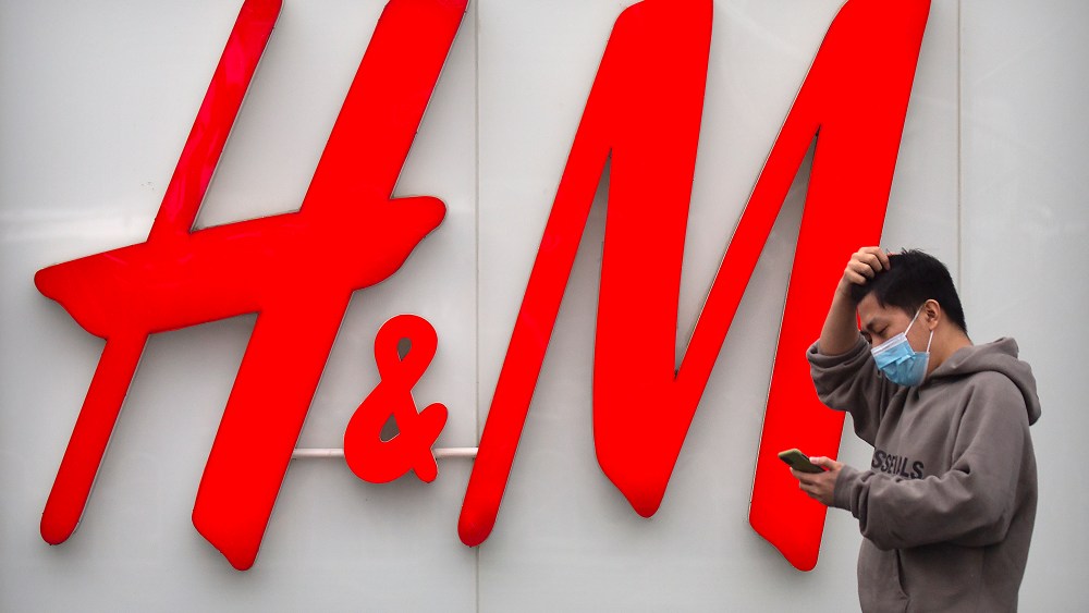 A man uses his smartphone as he walks past an H&M clothing store at a shopping mall in Beijing, Friday, March 26, 2021. H&M disappeared from the internet in China as the government raised pressure on shoe and clothing brands and announced sanctions Friday against British officials in a spiraling fight over complaints of abuses in the Xinjiang region. (AP Photo/Mark Schiefelbein)
