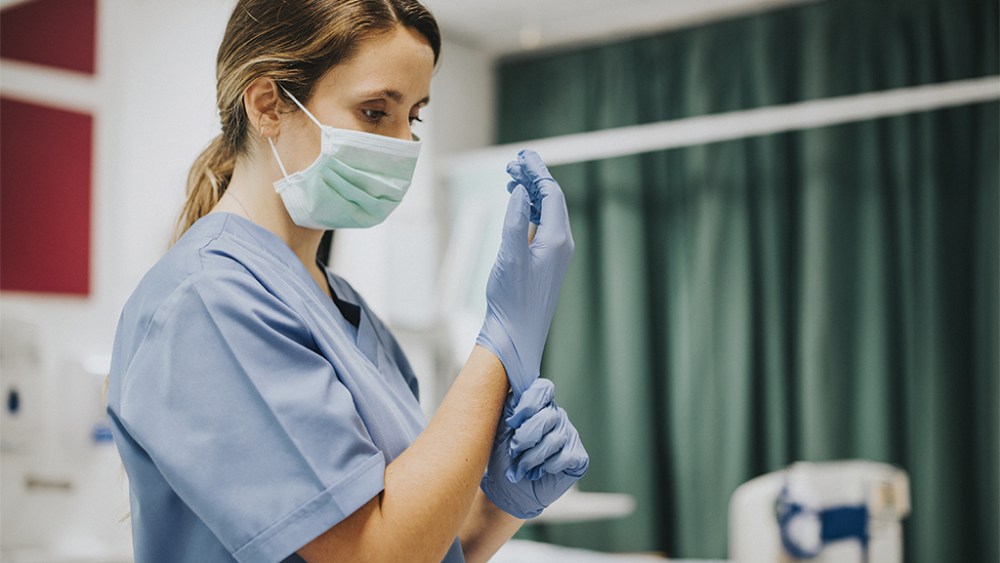 Female nurse with a mask putting on gloves