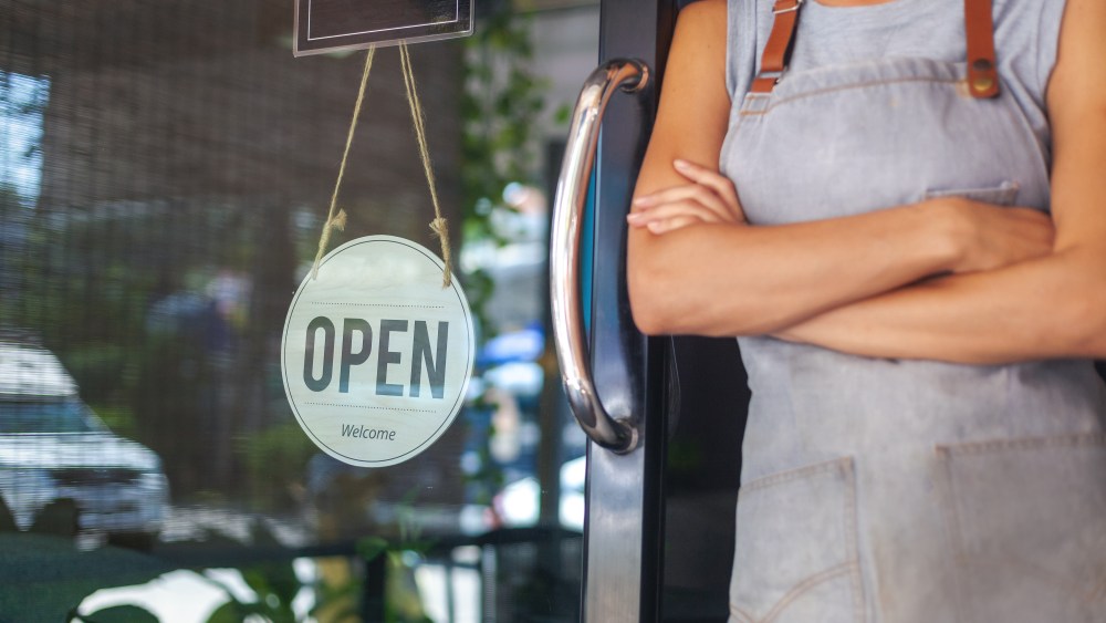 The woman is a waitress in an apron, the owner of the cafe stands at the door with a sign Open waiting for customers. Small business concept, cafes and restaurants