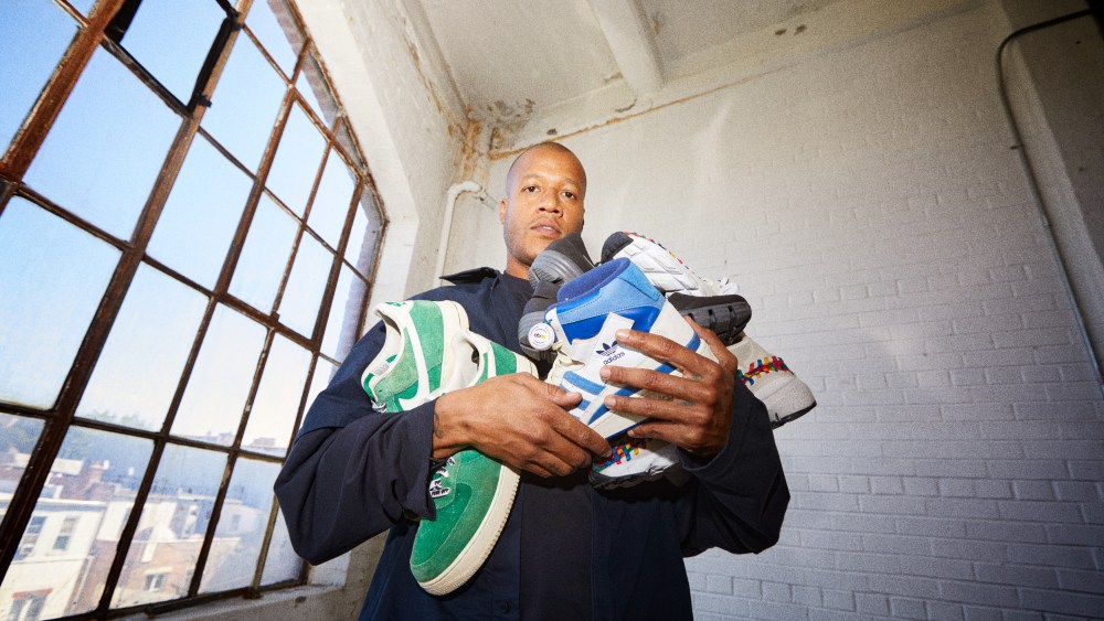 Heron Preston and eBay features the designer holding a bunch of colorful sneakers and standing next to a window with buildings in the background