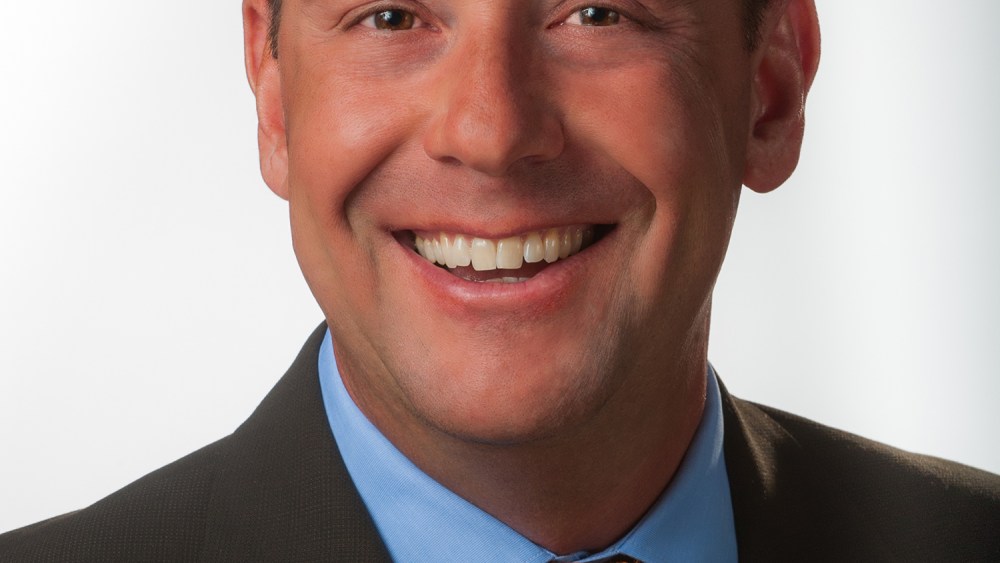 Scott Barnhart headshot wearing black suit, blue shirt, orange patterned tie.