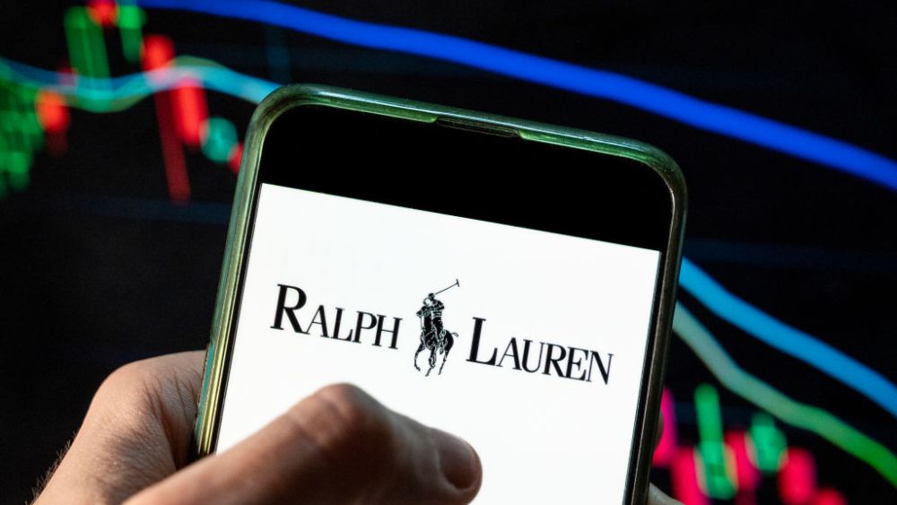 CHINA - 2021/12/09: In this photo illustration the American fashion brand Ralph Lauren logo seen displayed on a smartphone with an economic stock exchange index graph in the background. (Photo Illustration by Budrul Chukrut/SOPA Images/LightRocket via Getty Images)