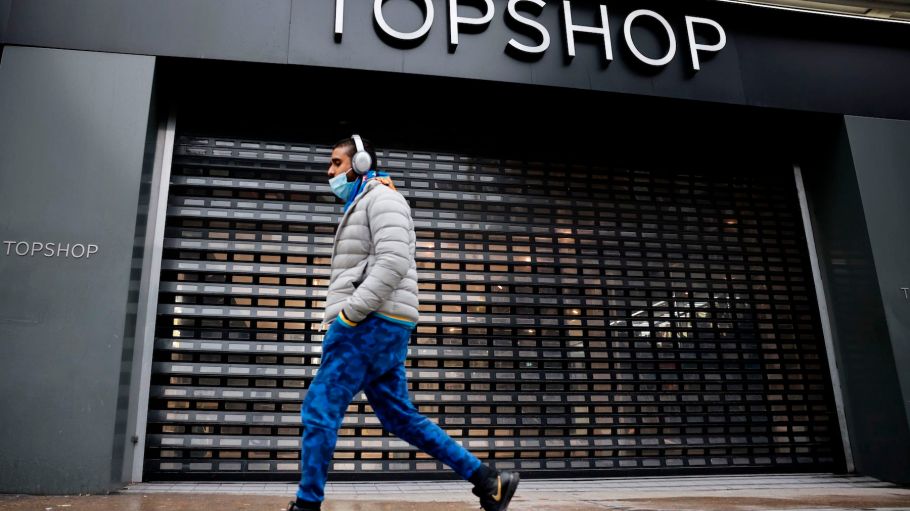 A pedestrian walks past the shuttered entrance of a closed-down Topshop fashion store is pictured trough a window in London on February 1, 2021. - Online clothing retailer ASOS bought Monday brands including Topshop from collapsed Arcadia but has snubbed its stores, resulting in around 2,500 job losses.