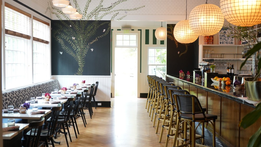 A view inside Christian's restaurant shows table seating and bar seating and large windows with lots of light.