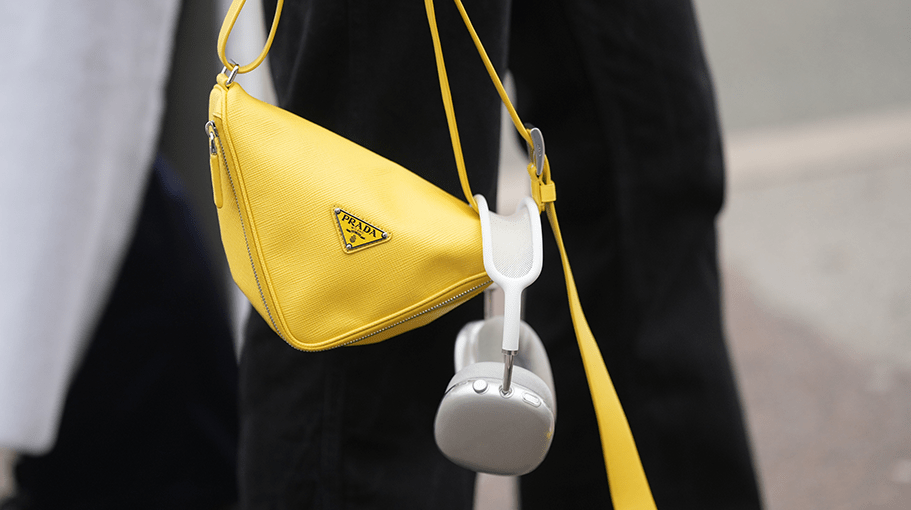 A guest wears silver rings, black denim wide legs pants, a yellow shiny leather Triangle handbag from Prada, white headphones , outside OperaSport , during the Copenhagen Fashion Week Autumn/Winter 2023 on February 01, 2023 in Copenhagen, Denmark.