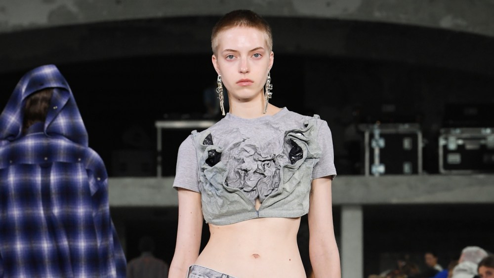 A model wears a cropped T-shirt and layered jeans on the runway at the Y/Project RTW Spring 2024 show.