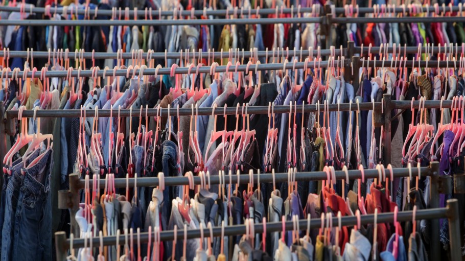 Huge selection of different used clothes for men, women and children on the rack in a second hand shop or thrift store. Concept of waste problem in fashion industry.
