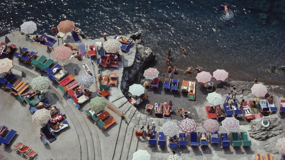 Elevated view looking down on sunbathers and parasols on the beach at La Scogliera beach in Positano, Italy, 1979.