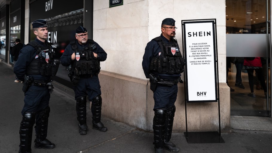 Riot police officers stand guard as people protest in front of the BHV department store in Paris, France, on November 5, 2025, on the opening day of Asian e-commerce giant Shein's first physical store outside the Bazar de l'Hotel de Ville (BHV) department store.
