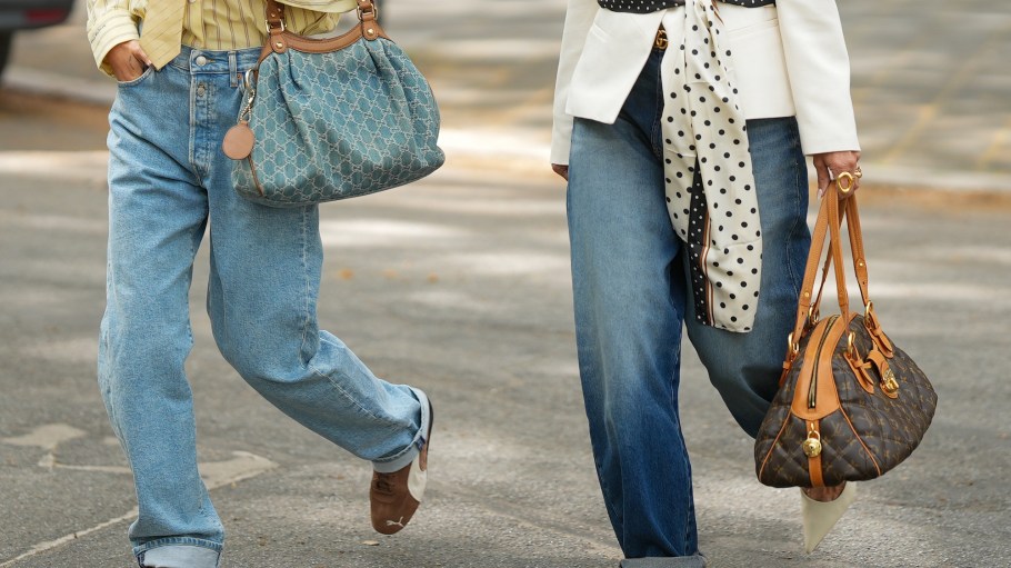 FRANKFURT AM MAIN, GERMANY - APRIL 21: Julia Kammerer (L) is seen wearing a yellow pinstripe button down shirt tucked into the pants from Pacific Republic; light wash straight leg jeans from Replay; brown leather "Speedboat" lace-up sneakers from Puma; a blue and beige "Gucci Denim GG Monogram Sukey Tote Bag" with tan leather trim and gold tone hardware from Gucci; a pale pink manicure; holding a red Coca Cola can; several chunky jewelry pieces in gold and silver including rings from Pandora, Akind, & other stories, H&M, my jewellery or scandiv;
Yvonne Schuppler-Kammerer (R) is seen wearing a white structured blazer with a shawl collar and padded shoulders from Zara; straight leg blue denim jeans with a folded hems from Zara; a cream and black polka dot scarf with a stripe border trim tied at the waist from H&M; a brown monogram canvas "Etoile Bowling Bag" with tan leather handles and gold tone hardware from Louis Vuitton; multiple gold rings from H&M; a nude manicure on April 21, 2026 in Frankfurt am Main, Germany. (Photo by Moritz Scholz/Getty Images)